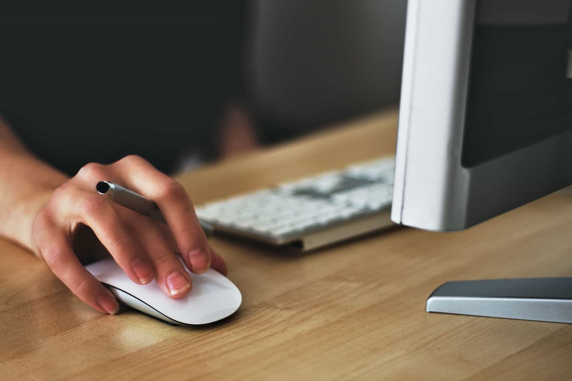 closeup of hand on mac mouse holding a stylus and using a computer